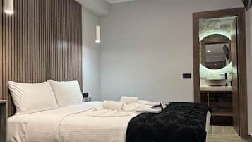 Un dormitorio moderno con una cama grande, un panel de madera decorativo, un espejo redondo y un baño visible al fondo.