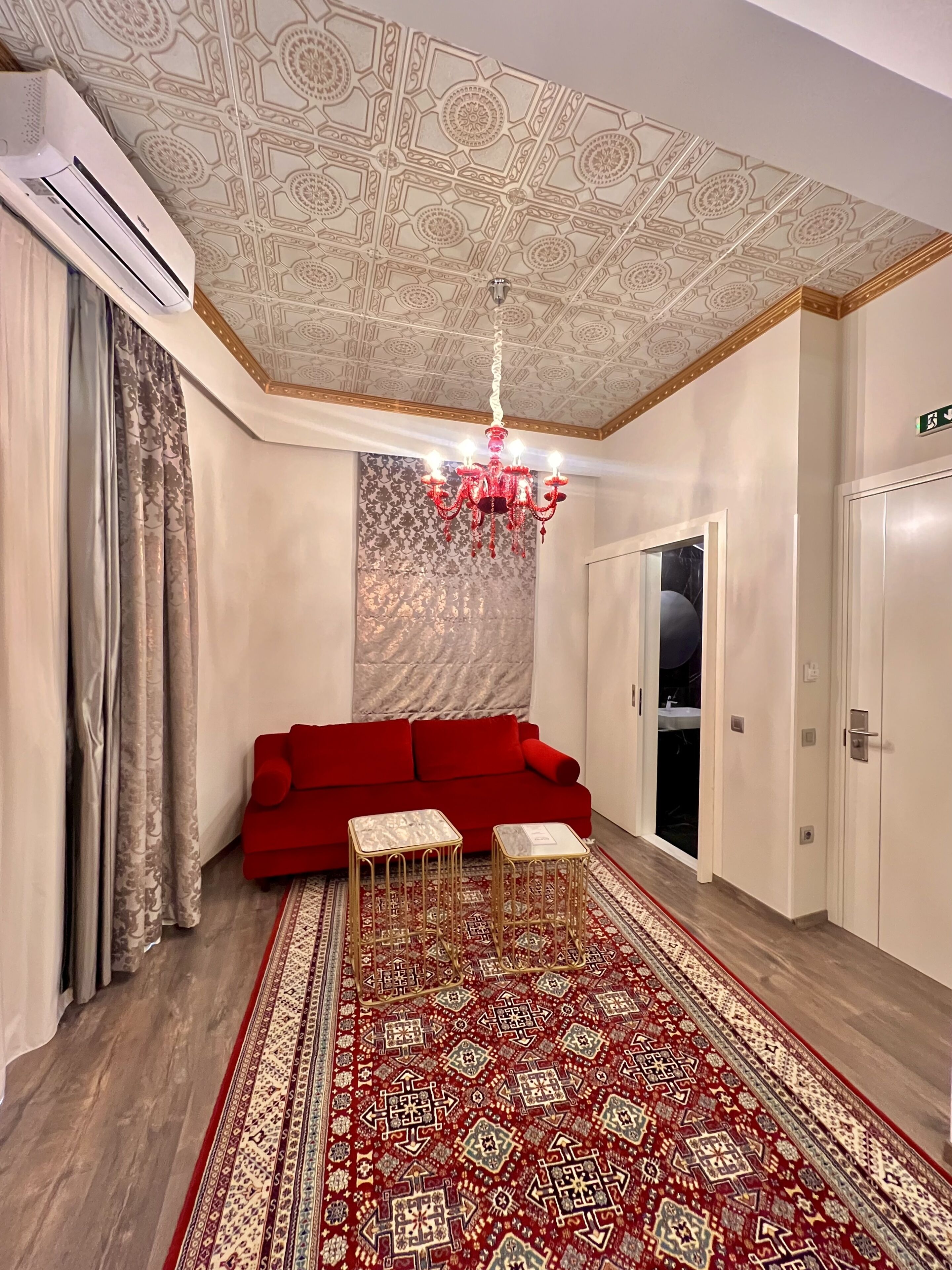 Una habitación con sofá rojo, alfombra estampada y una araña.
