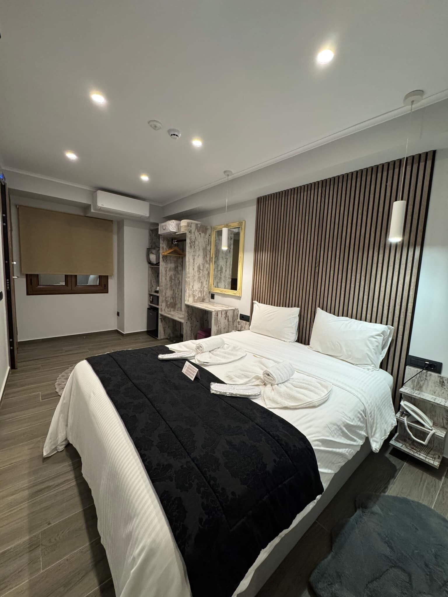 A modern bedroom with a large bed, a bedside table, a mirror, and a wardrobe.