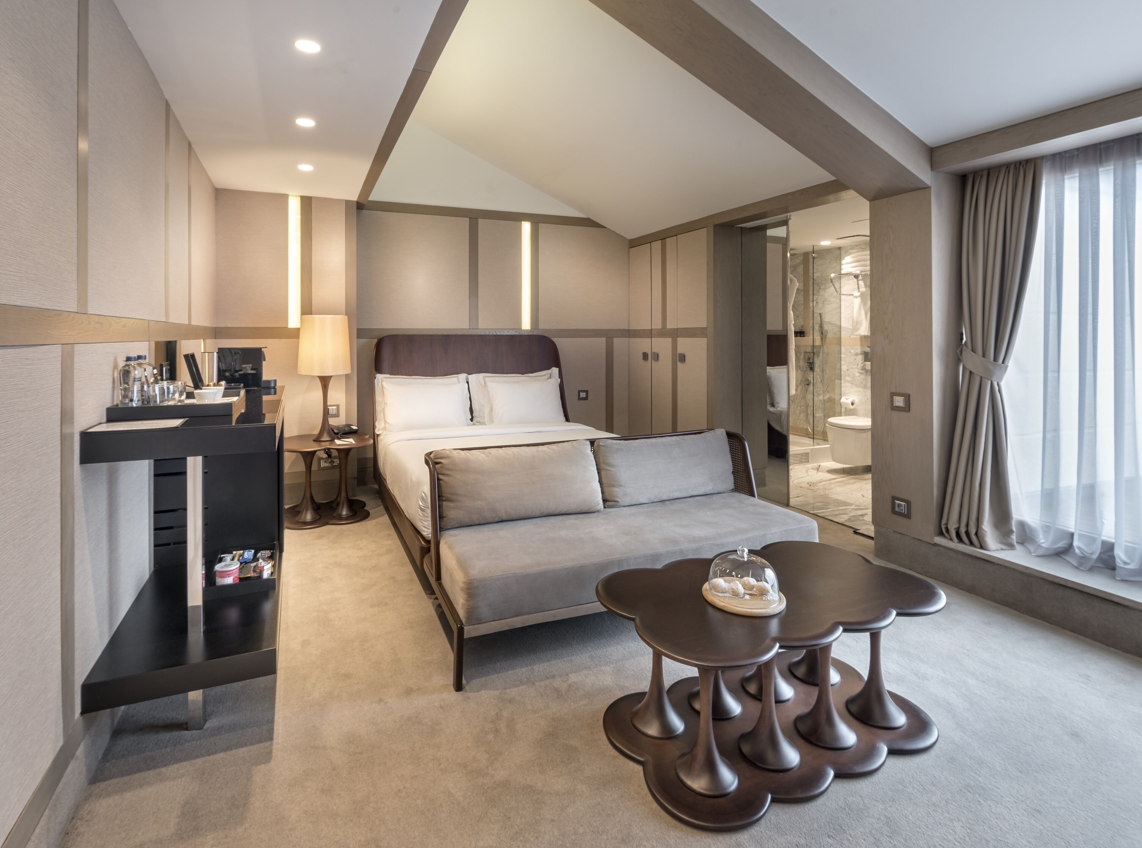 A modern hotel room with a large bed, bedside tables, a desk with a lamp, and a view of the bathroom.