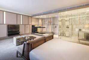 A modern hotel room with a large bed, a seating area with a sofa and a small table, a TV, a glass shower enclosure, and a view through the glass walls. - The Stay Nisantasi  (Istanbul)