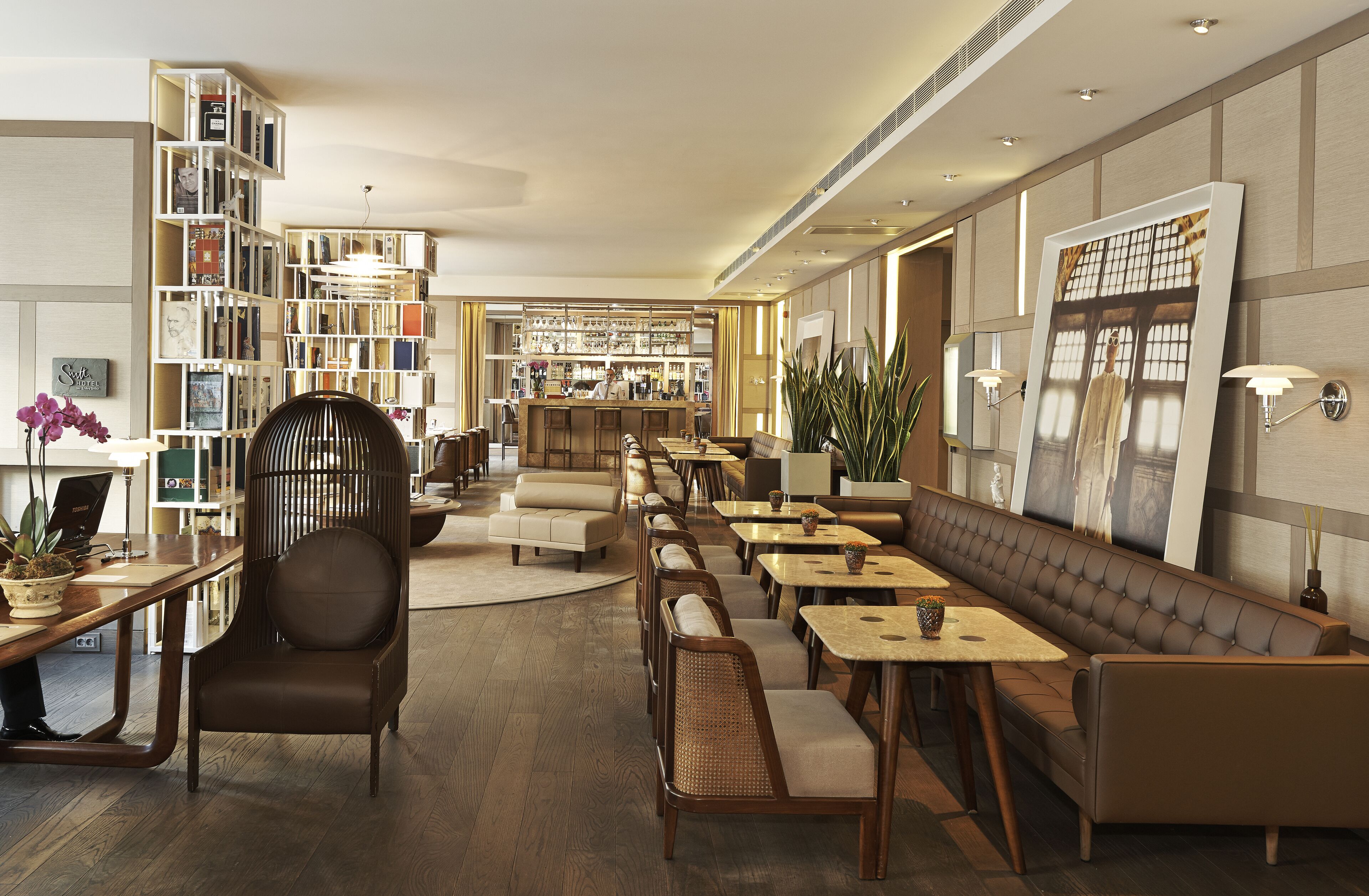 A modern hotel lobby with a long reception desk, seating areas, and a bookshelf filled with books.