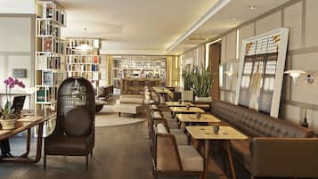 A modern hotel lobby with a long reception desk, seating areas, and a bookshelf filled with books.