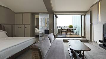 A modern hotel room with a bed, sofa, dining table, and a balcony with a view of the city.