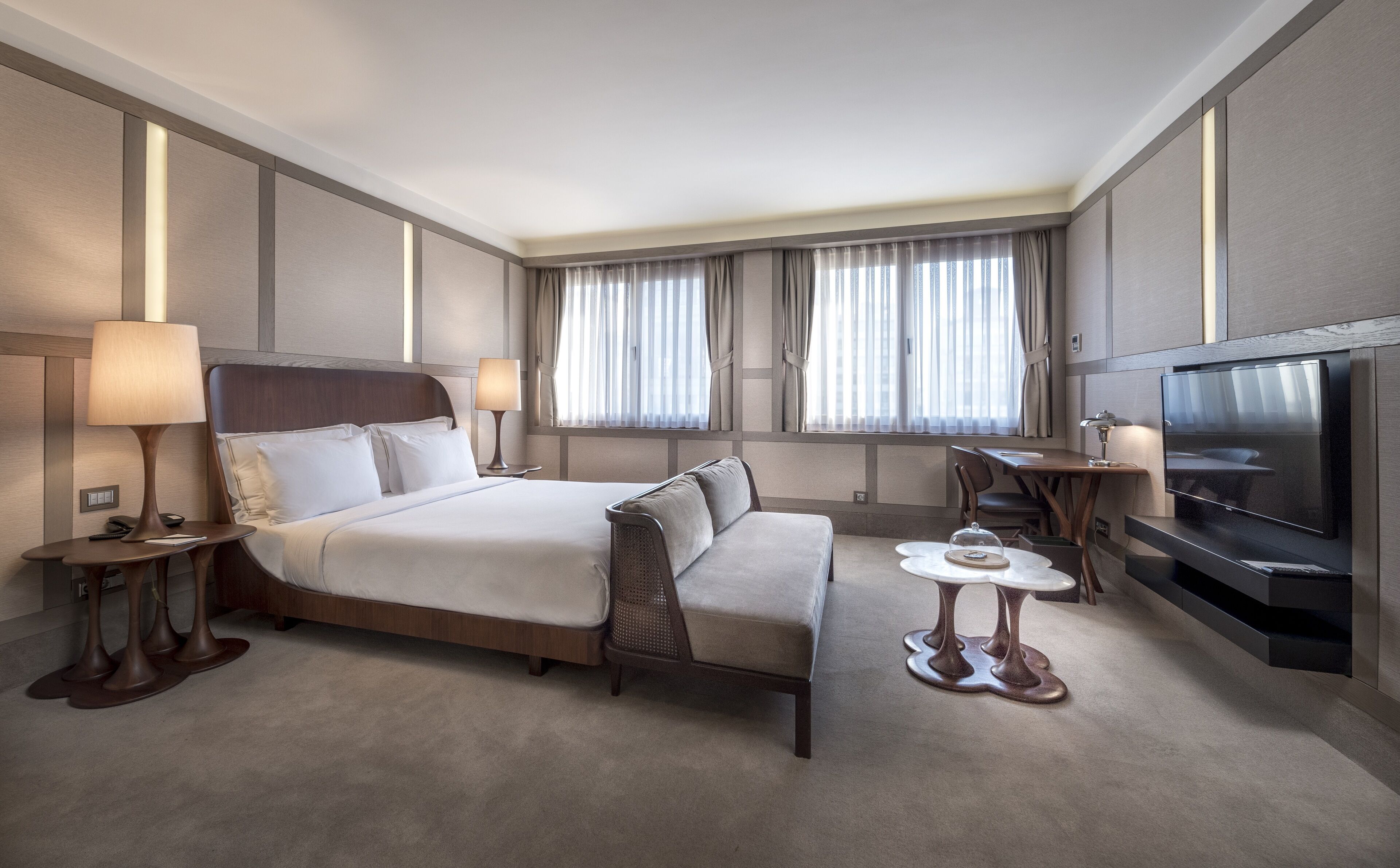 Una habitación de hotel con cama, sofá, escritorio, televisor y cortinas.