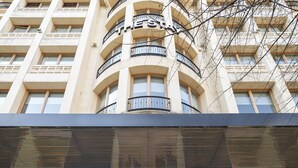 Η είσοδος ενός ξενοδοχείου με μοντέρνο σχεδιασμό, που διαθέτει μια γυάλινη πρόσοψη, μια εμφανή επιγραφή και ένα διακοσμητικό φωτιστικό σώμα.