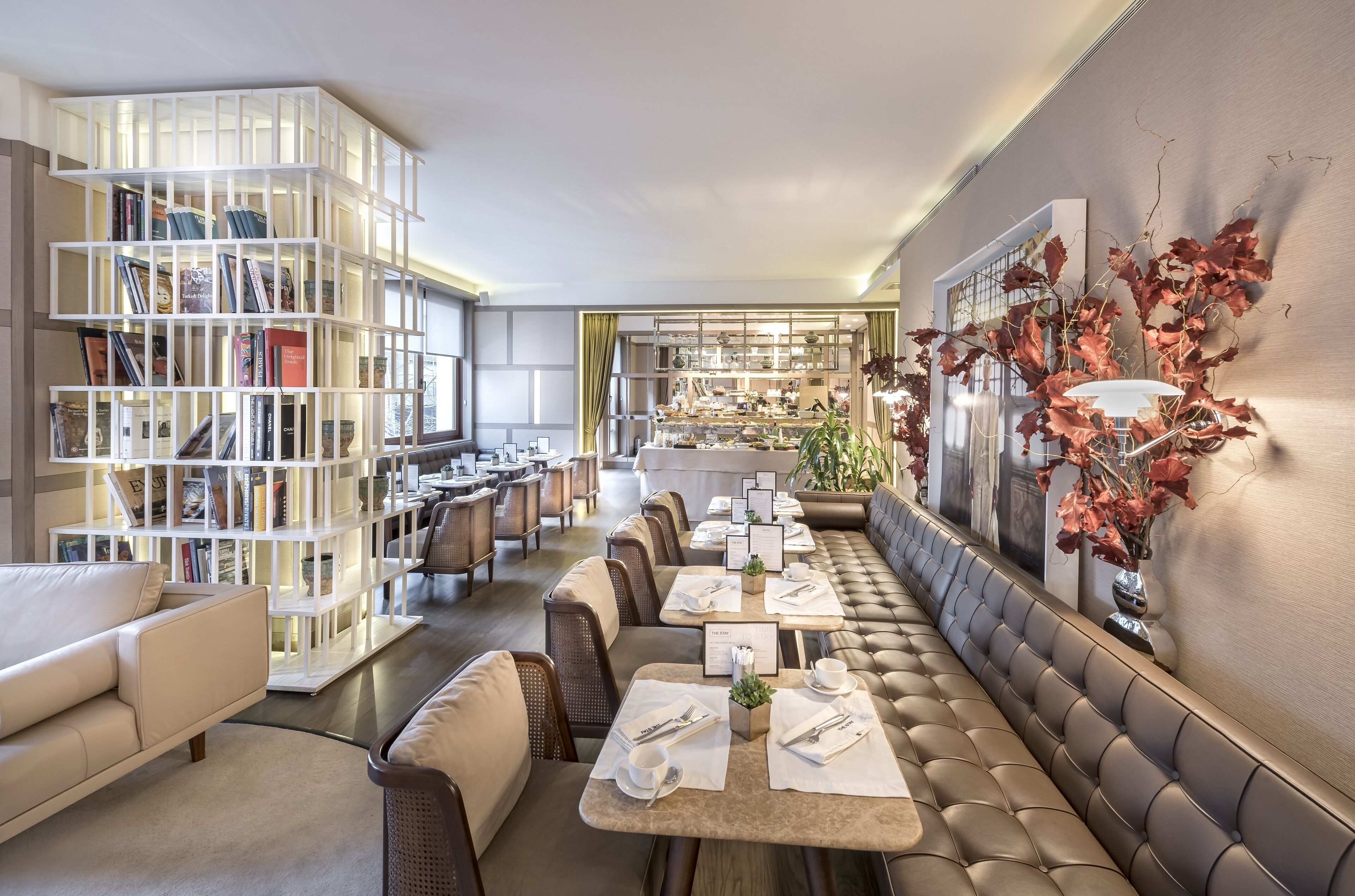 A modern dining area with a long bench, tables, and a bookshelf.