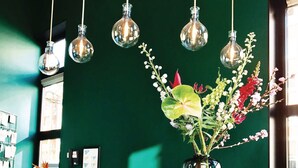 A reception area with a green wall, a white reception desk, and a vase of flowers. - Linden Hotel (Amsterdam)
