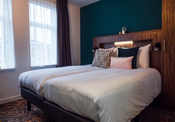 A hotel room with a large bed, a wooden headboard, and a view of the city through the window.