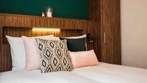 A neatly made bed with patterned and solid pillows, a wooden headboard, and a bedside lamp. - Linden Hotel (Amsterdam)