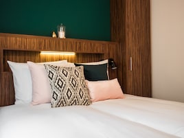 Un lit bien fait, agrémenté d’oreillers à motifs et unis, d’une tête de lit en bois et d’une lampe de chevet.