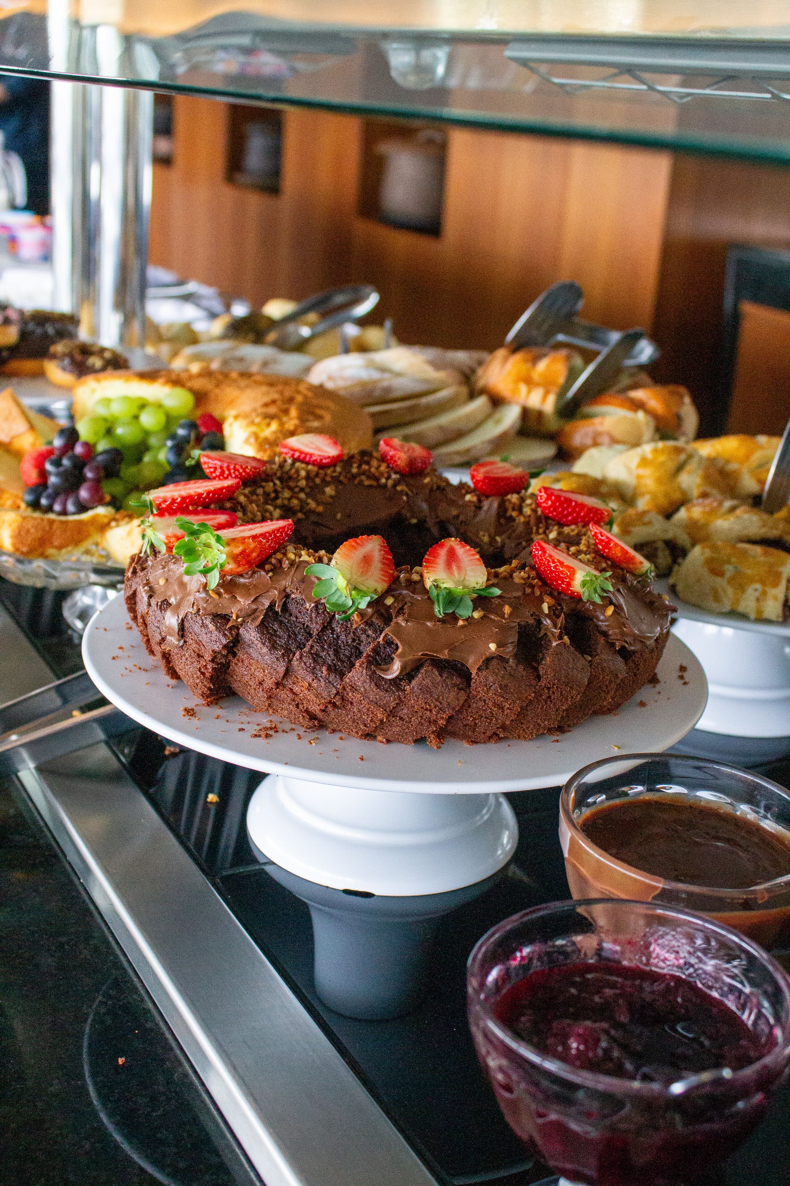 A display of various desserts including a chocolate cake with strawberries, a glass of berry compote, and assorted pastries.