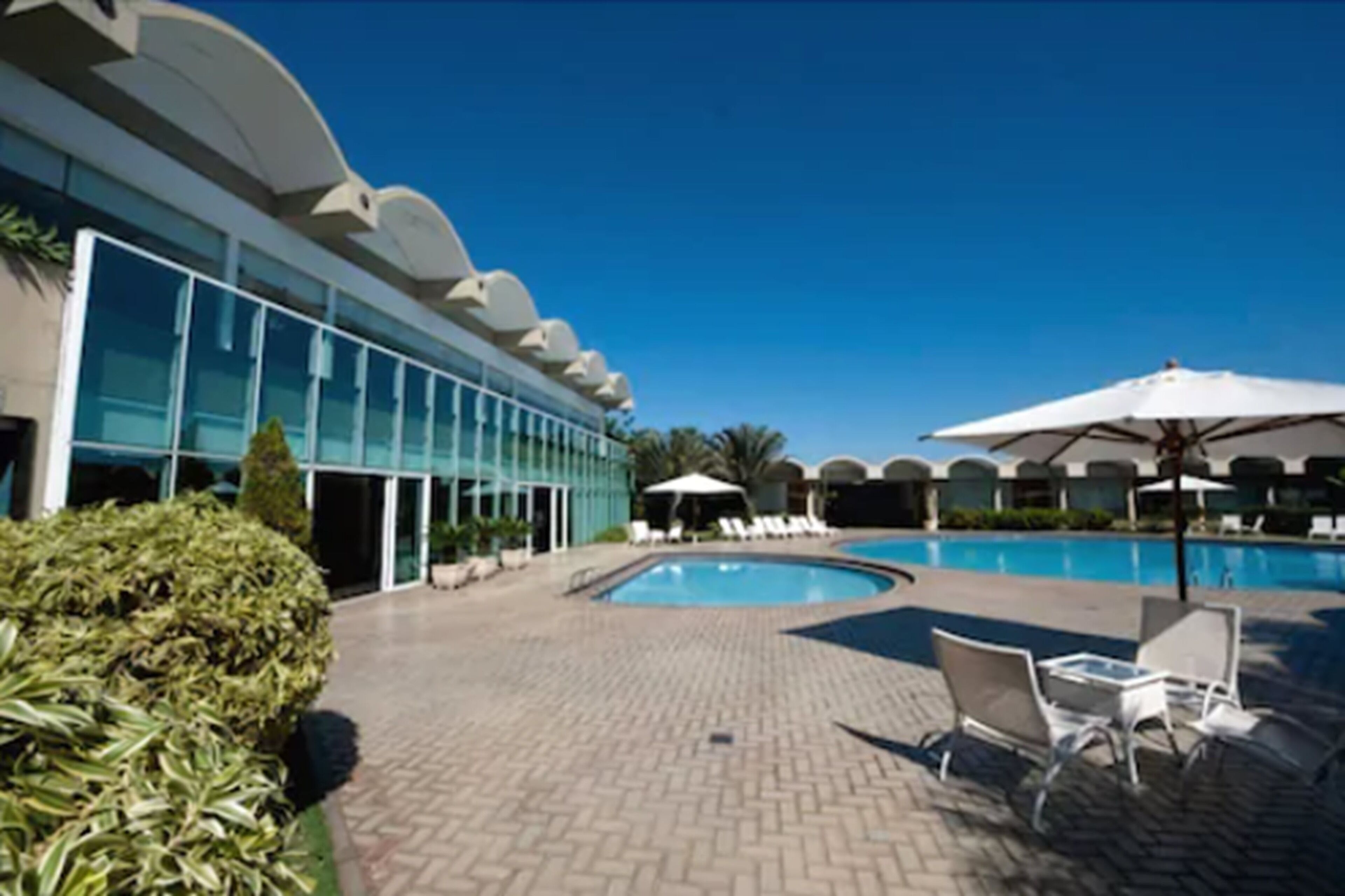 A modern hotel with a swimming pool, lounge chairs, and umbrellas.