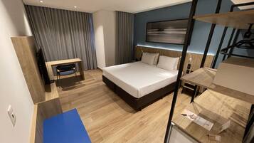 A modern hotel room with a large bed, a desk, a chair, and a wardrobe.