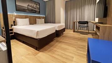 Quarto de hotel com duas camas, uma escrivaninha, uma cadeira, uma televisão e um quadro na parede.