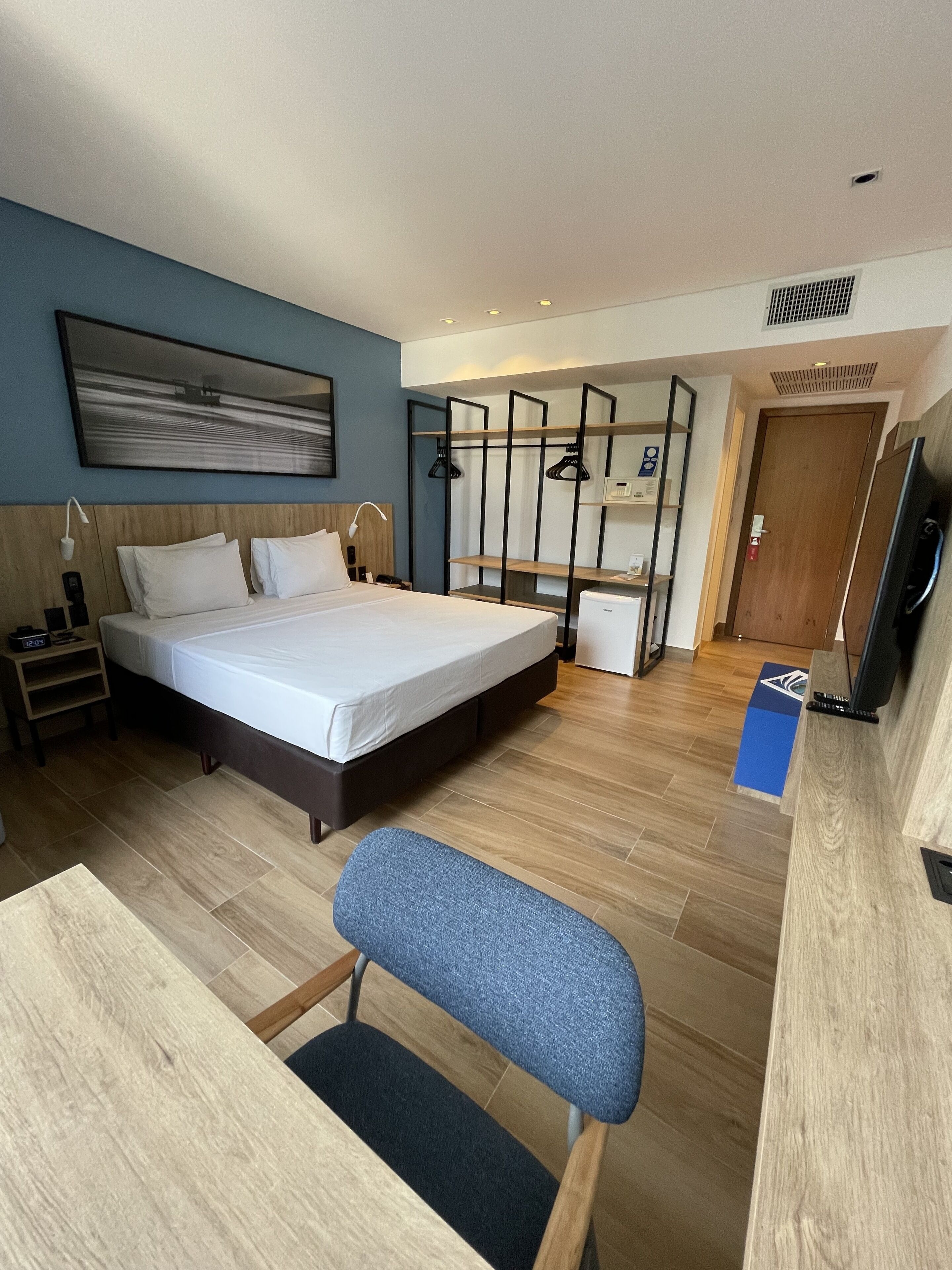 A hotel room with a bed, bedside table, lamp, and a desk with a chair.