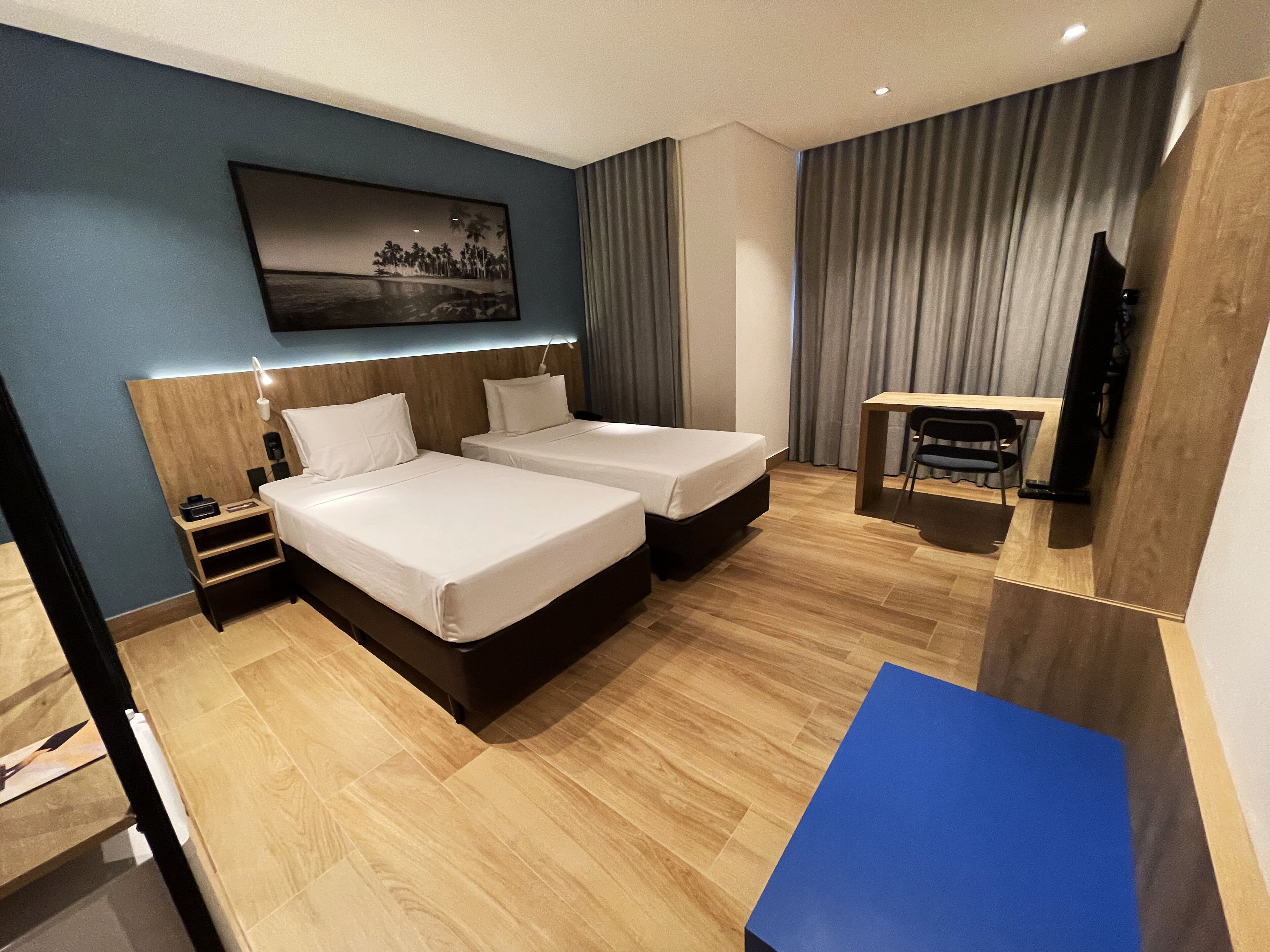 Hotelkamer met twee bedden, een bureau, een stoel, een televisie en een schilderij aan de muur.