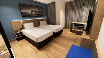 Hotelkamer met twee bedden, een bureau, een stoel, een televisie en een schilderij aan de muur.