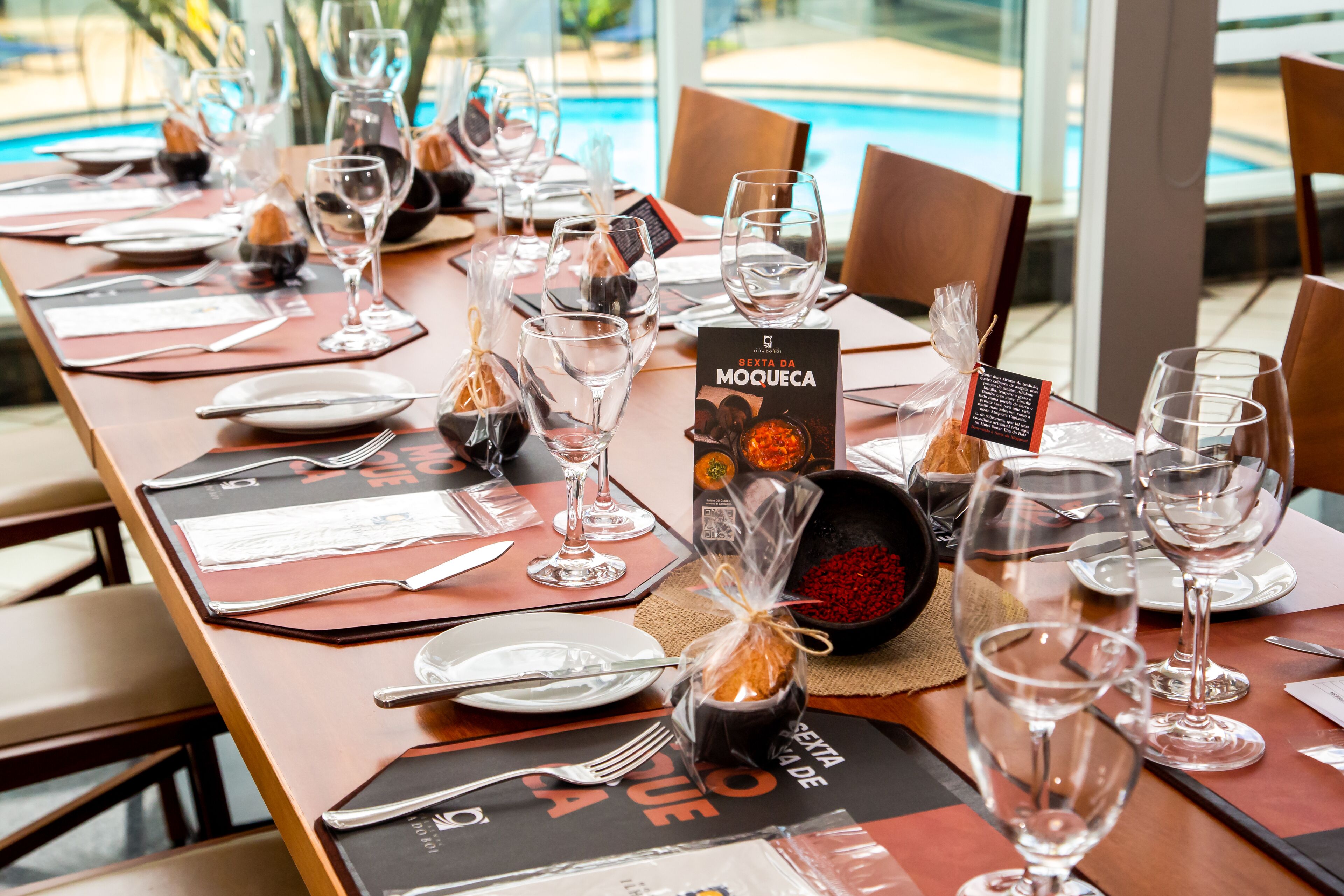 Una mesa de comedor dispuesta con copas de vino, platos y cubiertos, un atril para el menú y un centro de mesa decorativo.