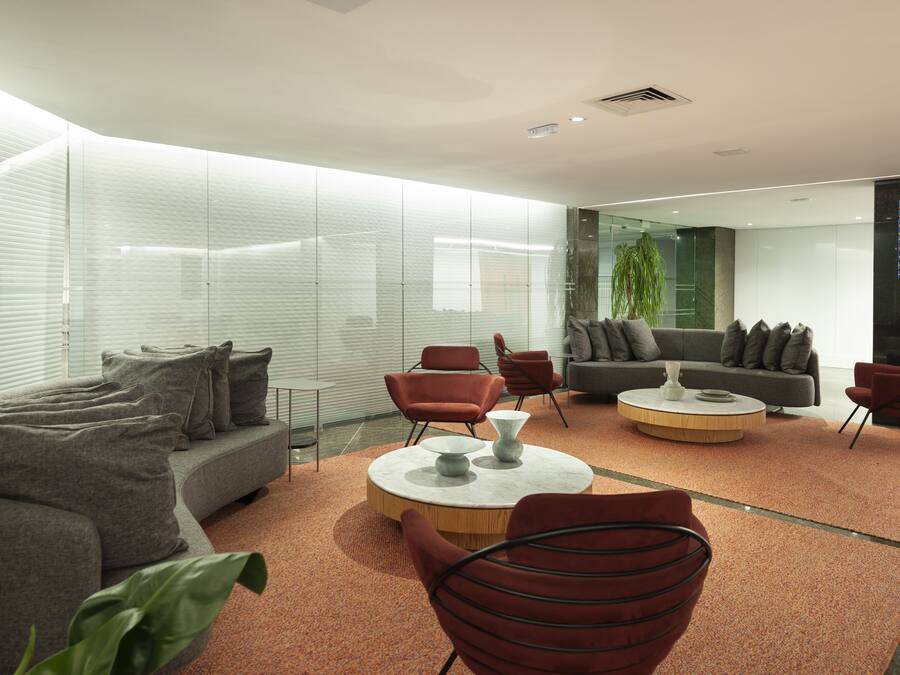 A modern interior with a grey sofa, red chairs, a round coffee table, and a glass wall.