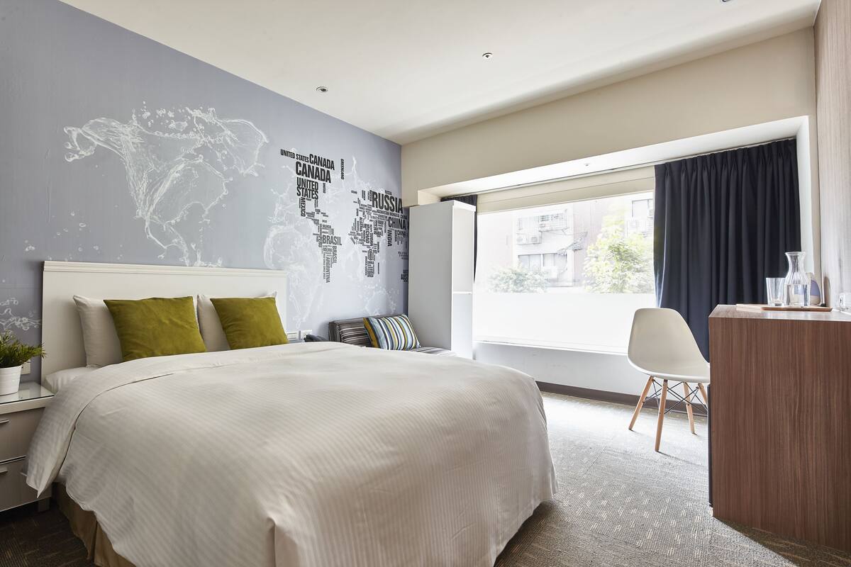 A modern hotel room with a large bed, a desk, and a view of the city.