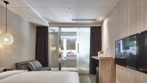 A modern hotel room with a large bed, a desk with a flat-screen TV, a glass shower enclosure, and a view of the bathroom. - Via Hotel Loft (Taipei)