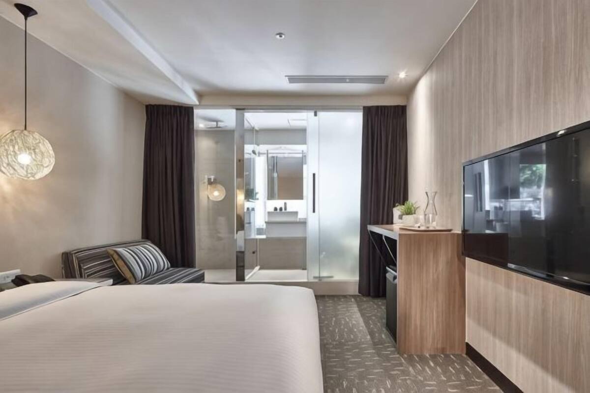 A hotel room with a bed, a TV, a desk, and a sliding glass door leading to a bathroom.