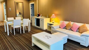 A hotel room with a dining area, a sofa with cushions, a coffee machine, a lamp, and a mirror. - La Vie En Rose Hotel (Chiang Rai)