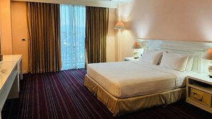 Ein Hotelzimmer mit einem großen Bett, einem Schreibtisch, einem Stuhl, einer Lampe und einem Fenster mit Vorhängen.