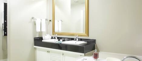 A modern bathroom with a large bathtub filled with bubbles, a black countertop with a white sink, and a gold-framed mirror.