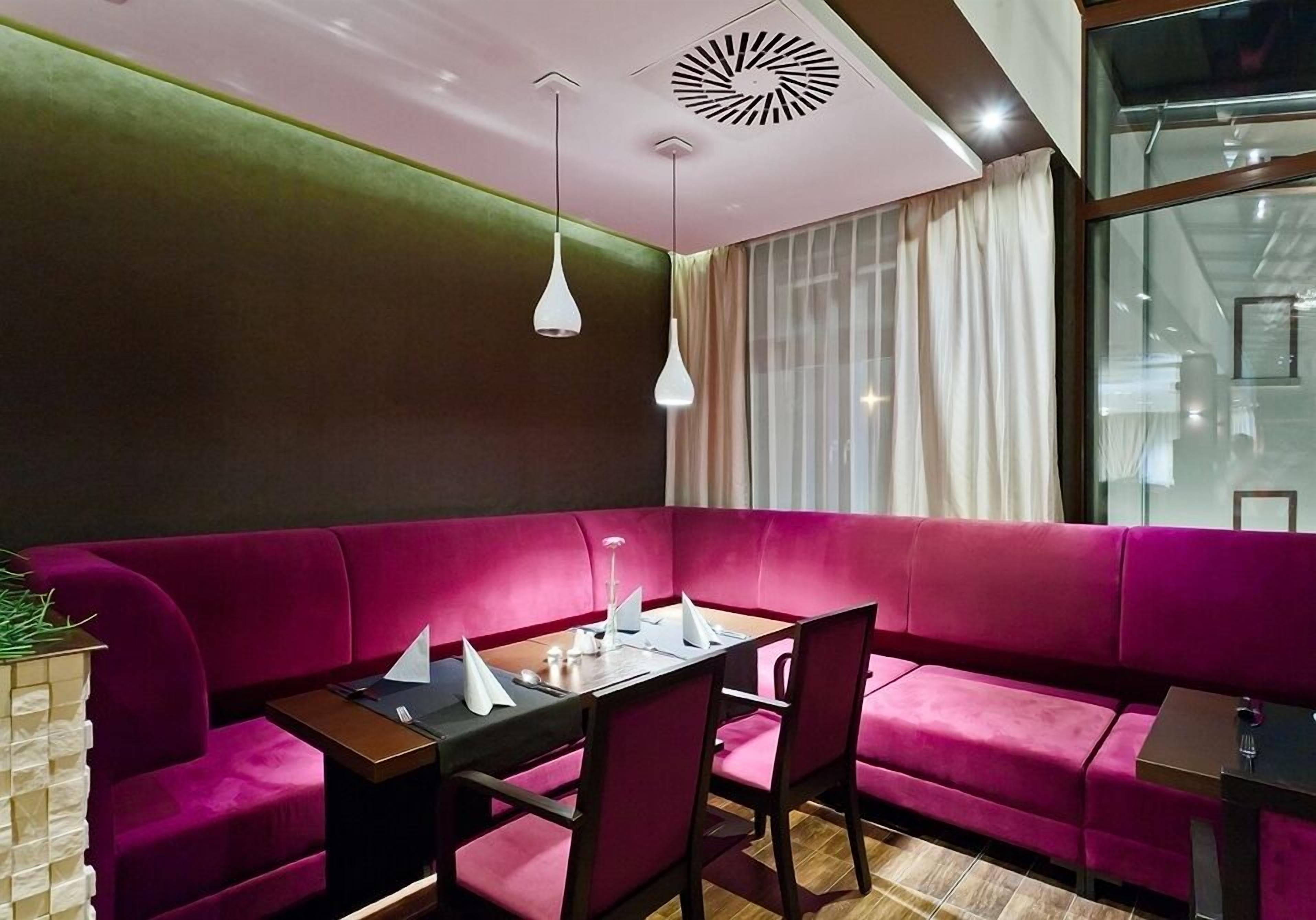 A modern dining area with a pink sofa, a wooden table, and white pendant lights.