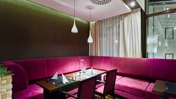 A modern dining area with a pink sofa, a wooden table, and white pendant lights.