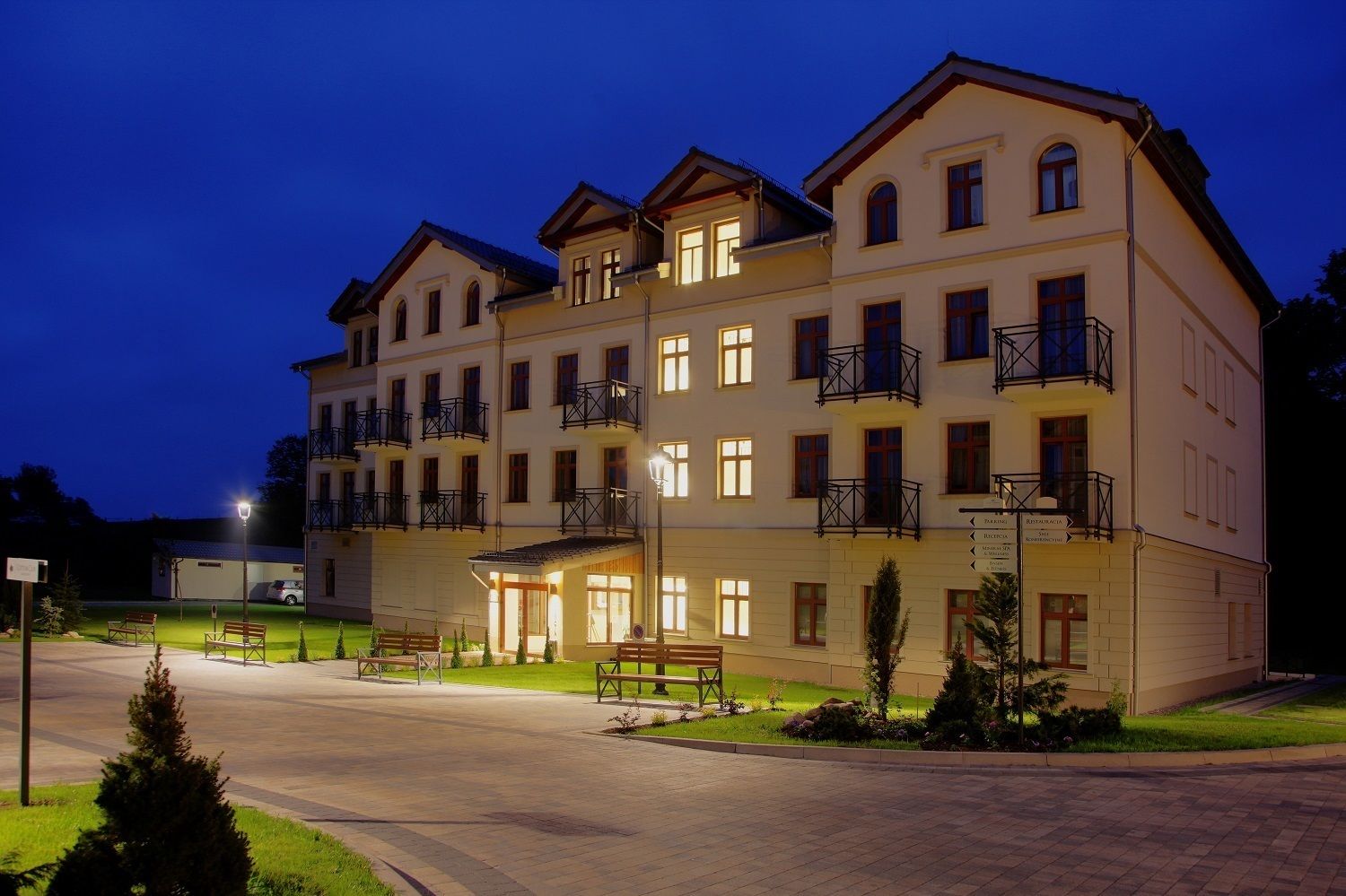 A multi-story hotel with a well-lit entrance, outdoor seating, and a parking area.