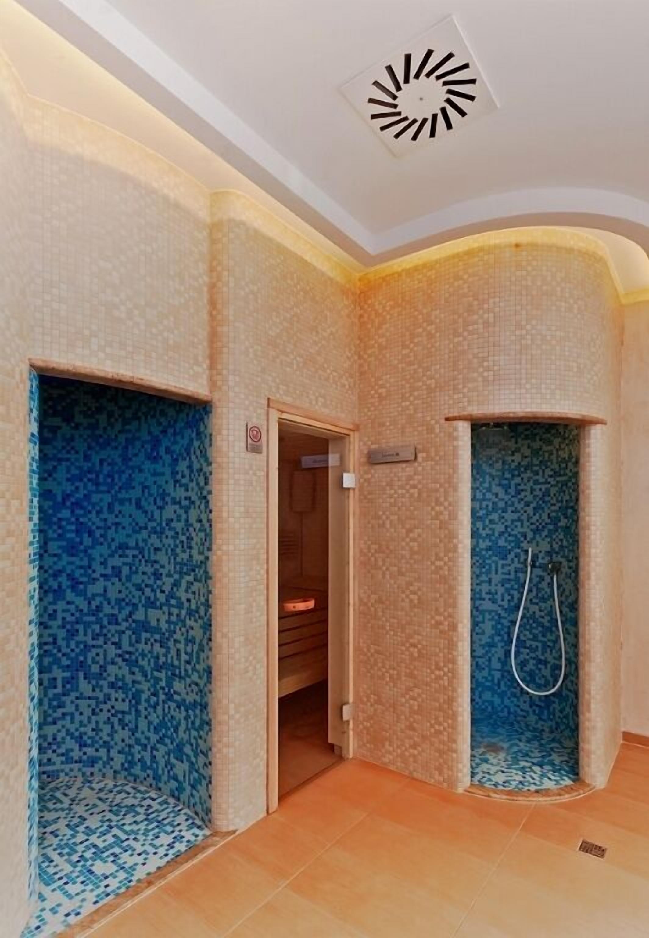 Un baño con paredes de mosaicos, zona de ducha y una puerta visible que conduce a otra habitación.