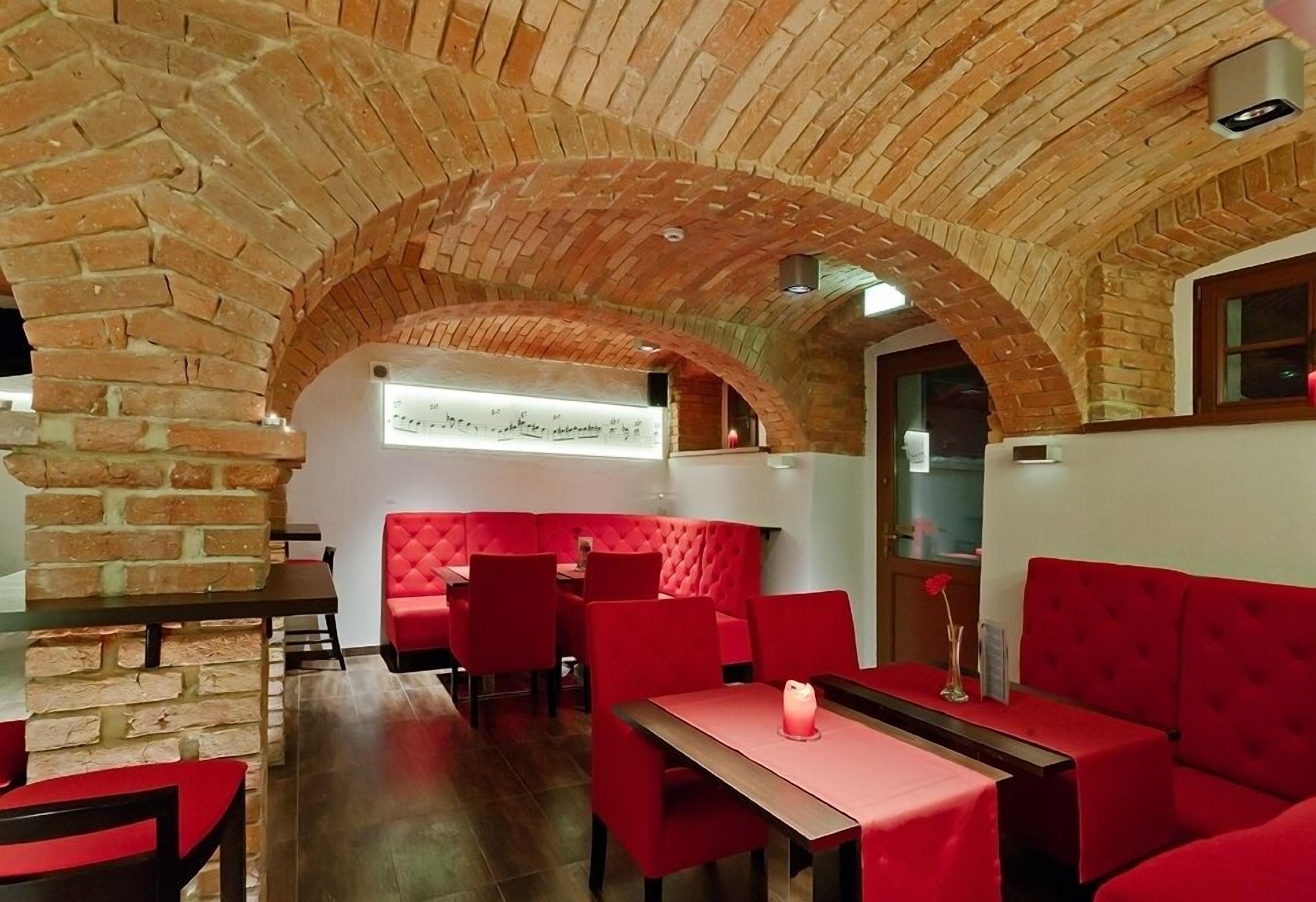 A restaurant with brick arches, red seating, and a checkered tablecloth.