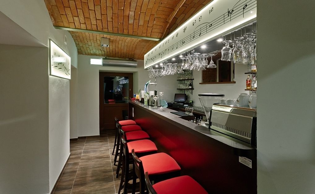 A bar area with red bar stools, a counter with a cash register, and hanging glassware.