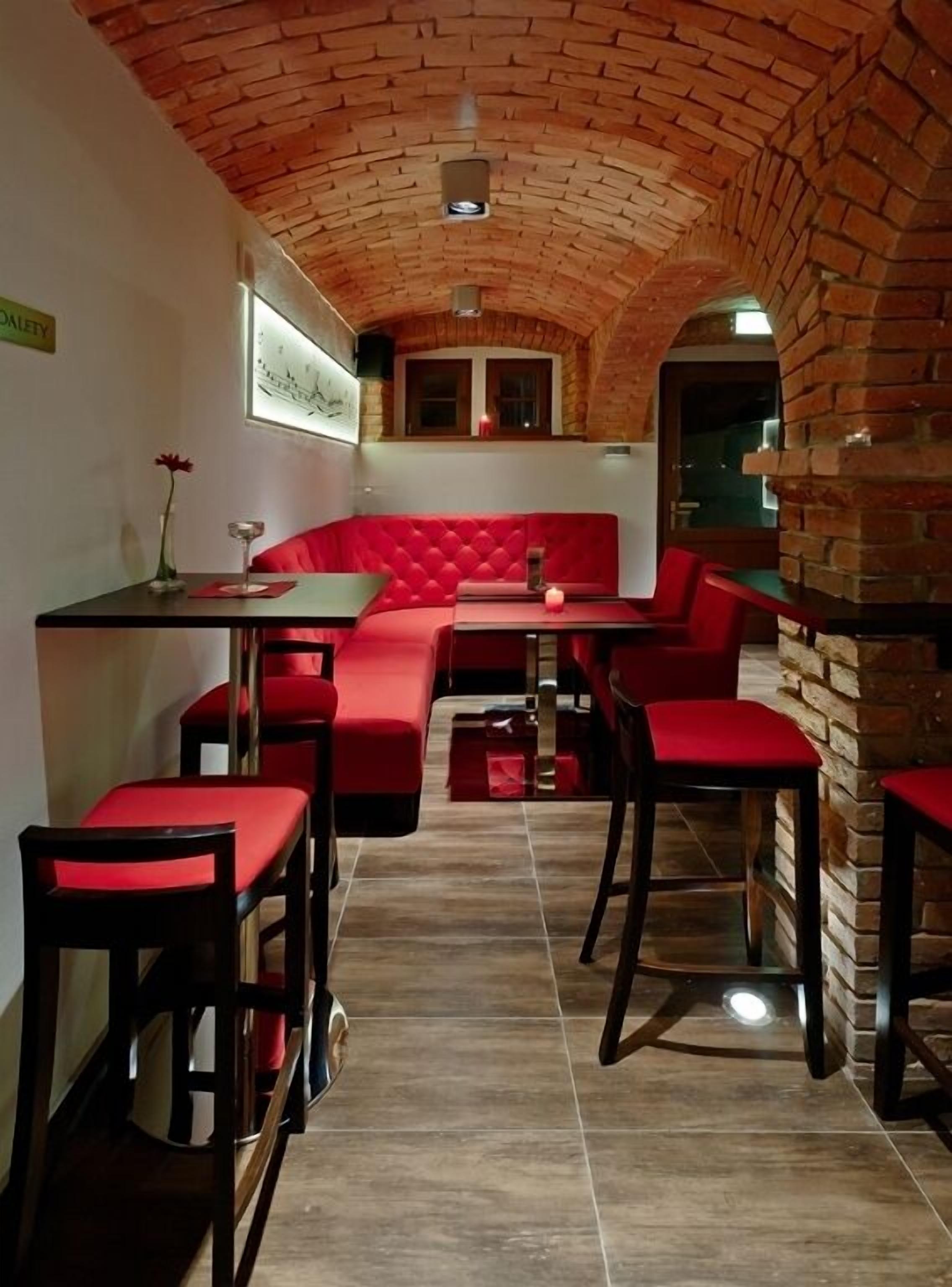 A cozy restaurant with a brick arch ceiling, red cushioned seating, and a tiled floor.