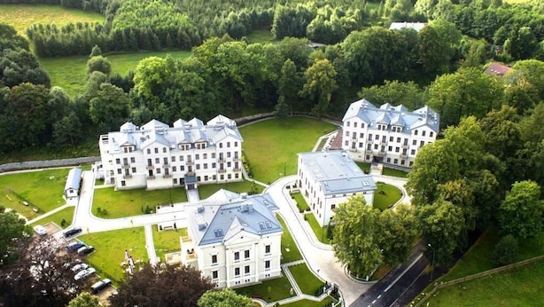 A large, white, multi-story building complex with a symmetrical layout, surrounded by lush greenery and a well-maintained lawn. - Cottonina Hotel & Mineral SPA Resort (Swieradow-Zdroj)
