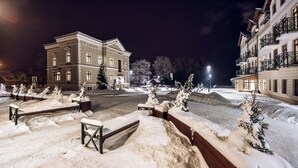 A snow-covered courtyard with benches and a building with balconies. - Cottonina Hotel & Mineral SPA Resort (Swieradow-Zdroj)