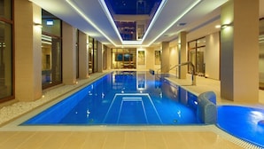 A modern indoor swimming pool with a clear blue water surface, surrounded by a tiled floor and walls, and illuminated by overhead lighting. - Cottonina Hotel & Mineral SPA Resort (Swieradow-Zdroj)