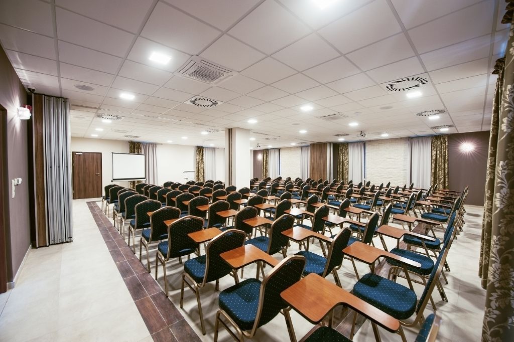 A conference room with rows of desks and chairs, a whiteboard, and a projector screen.
