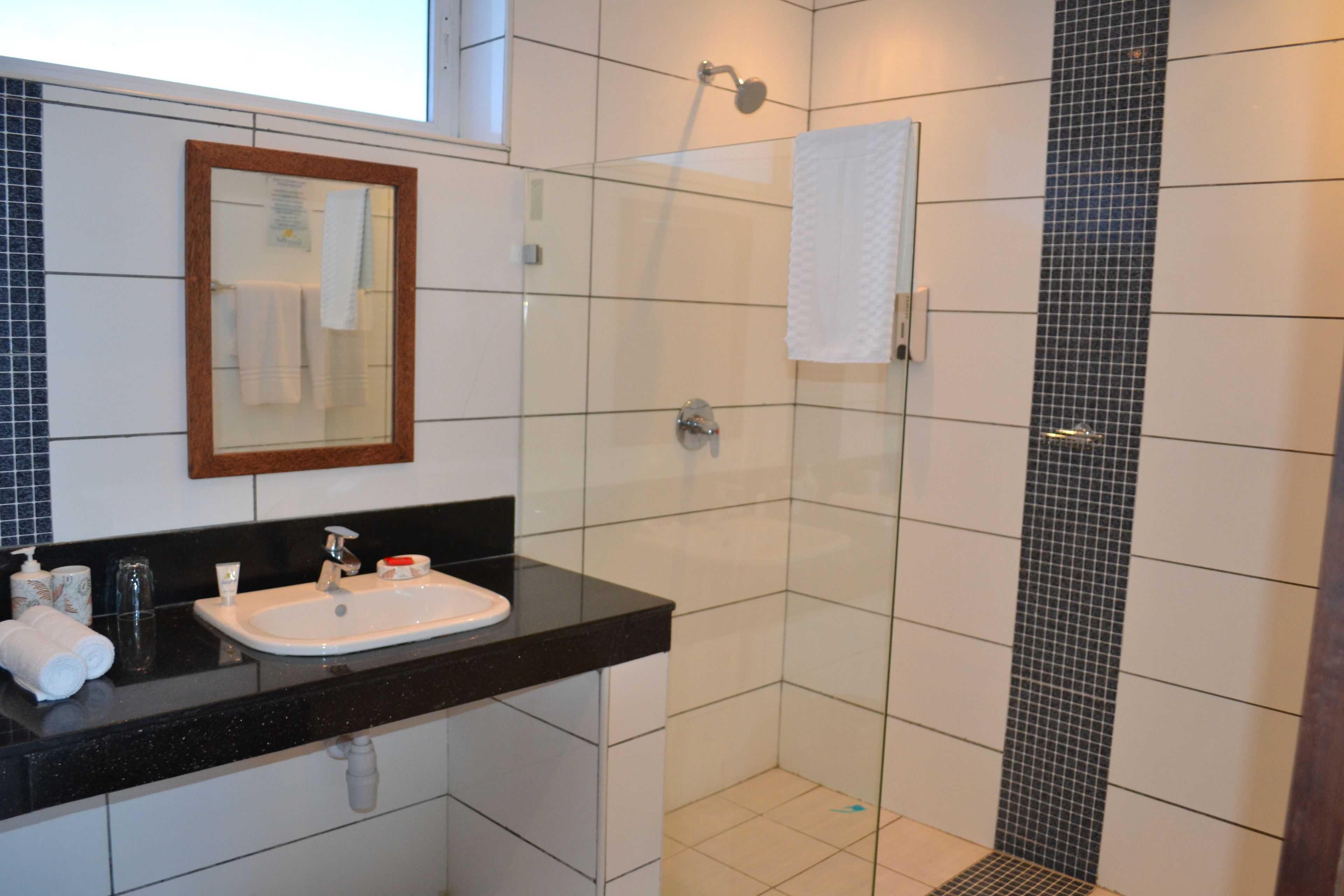 Ein Badezimmer mit schwarzem Waschtisch, einem Spiegel und einer Duschkabine mit gefliesten Wänden.