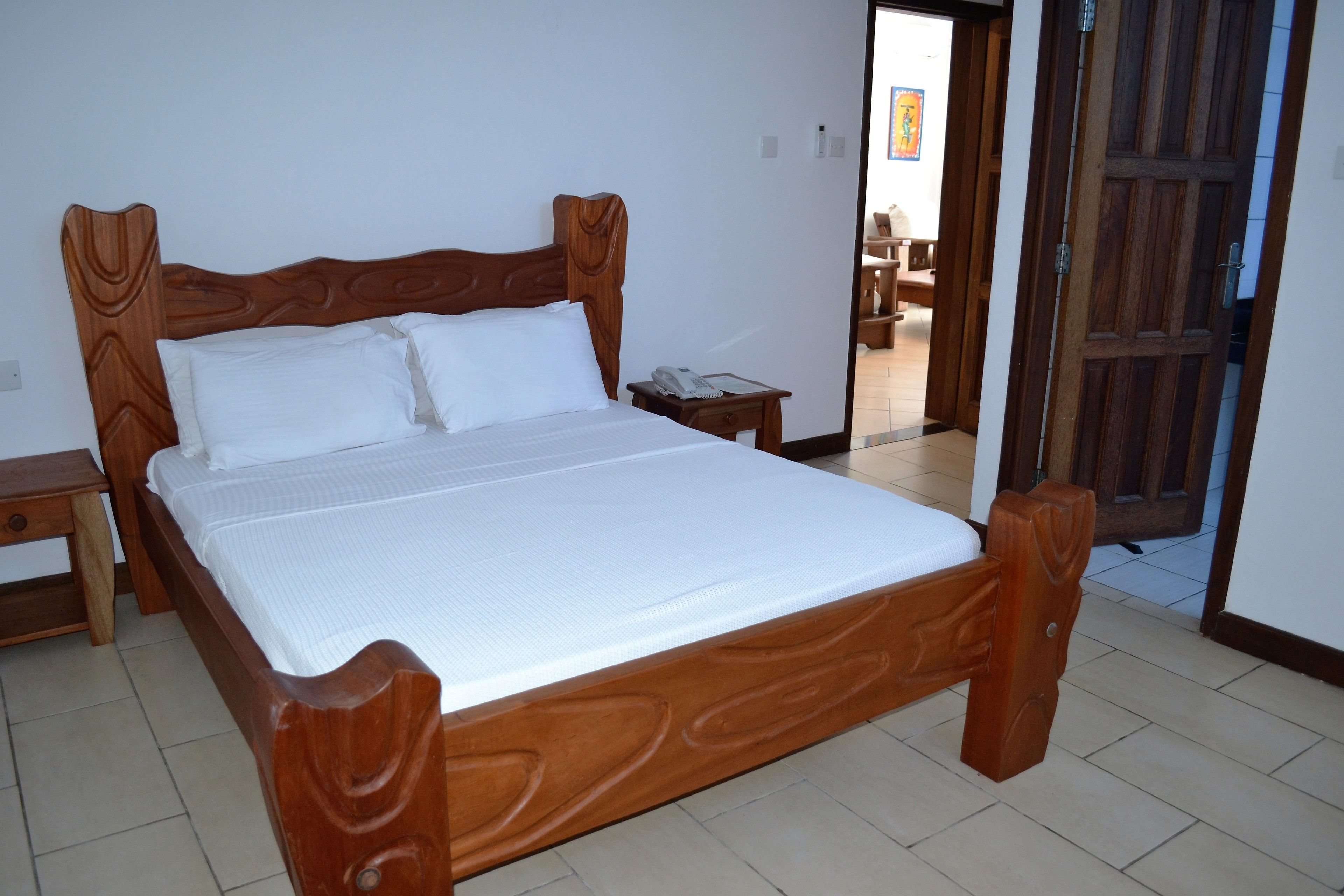 A wooden bed with white bedding in a room with tiled flooring.