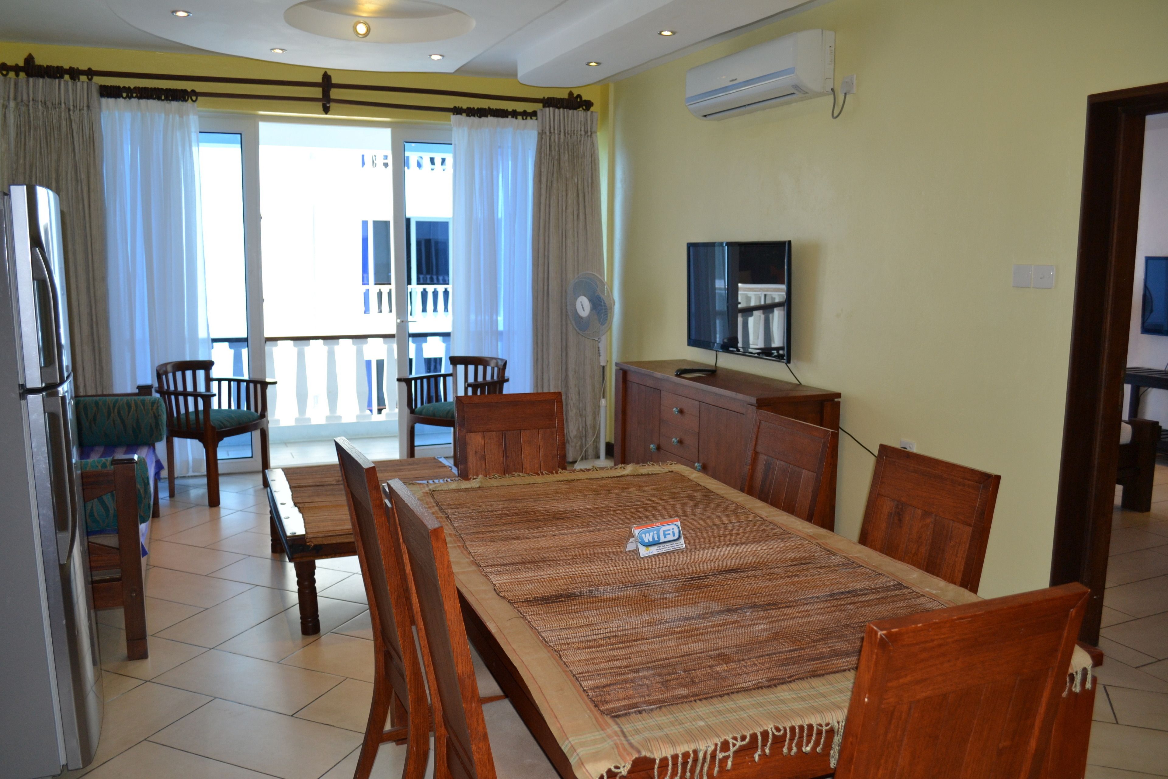 A dining area with a large wooden table, chairs, and a TV on the wall.
