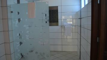 Een badkamer met witte betegelde wanden, een glazen wand met abstracte uitsparingen, een handdoekrek en een raam dat natuurlijk licht binnenlaat.