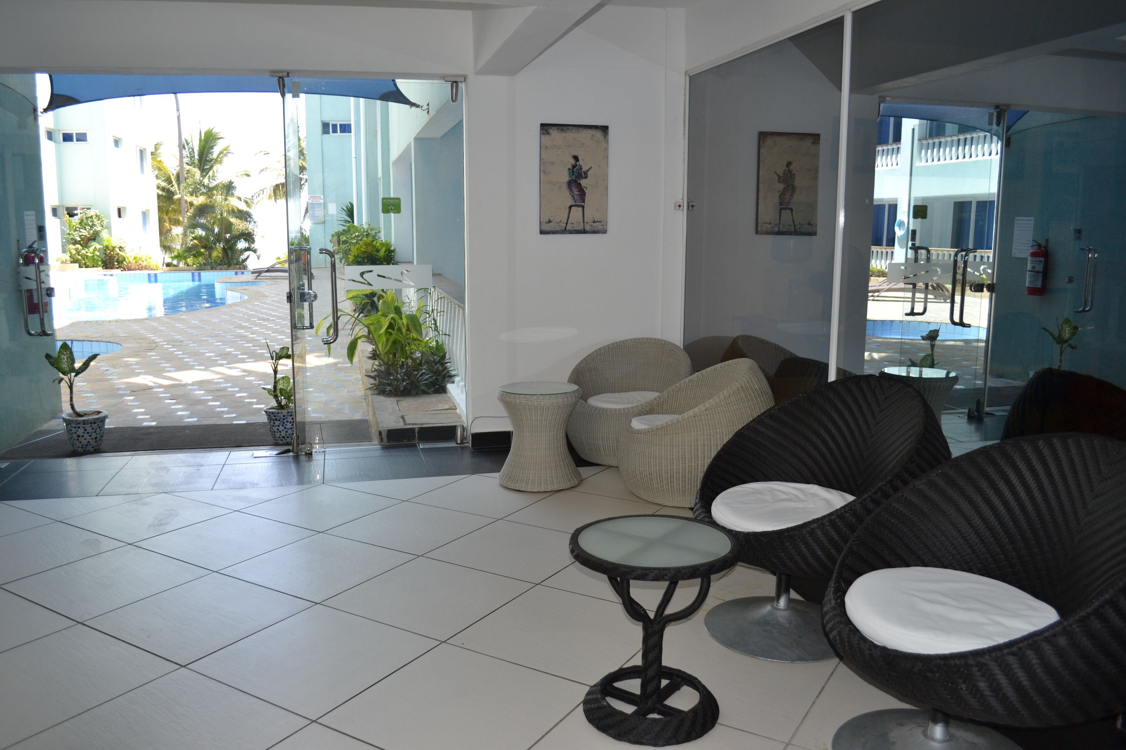 A modern hotel lobby with a pool view, wicker furniture, and potted plants.