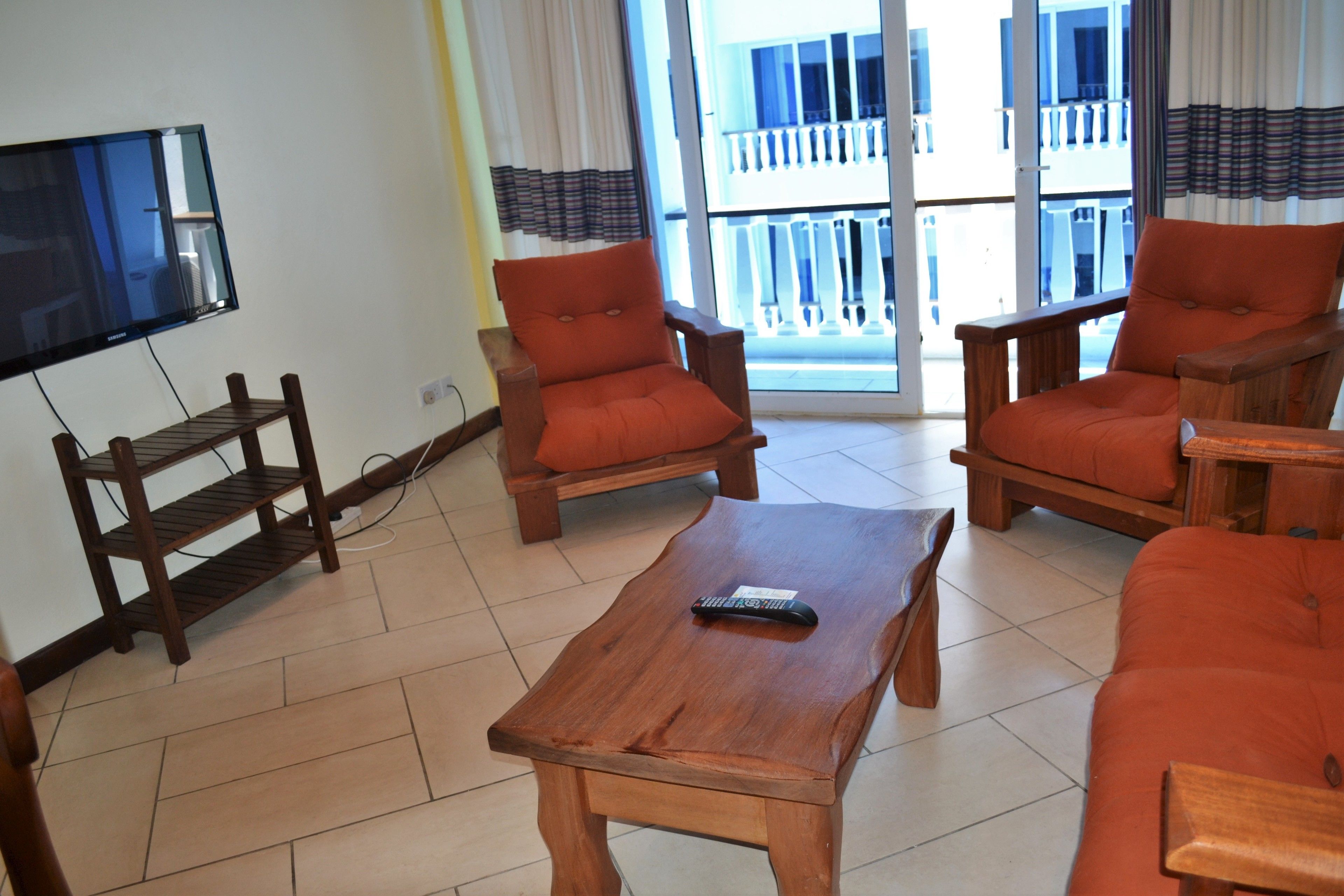 A living room with a wooden coffee table, two orange armchairs, and a TV mounted on the wall.