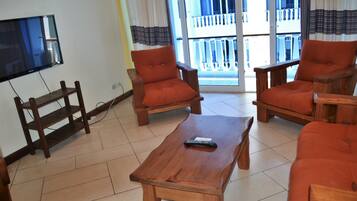 A living room with a wooden coffee table, two orange armchairs, and a TV mounted on the wall.