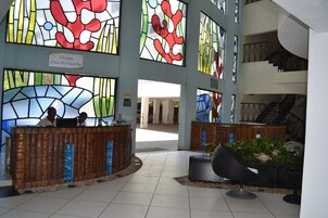 Zona de recepción con un mostrador de madera, una escalera y amplios ventanales de vidrio emplomado.