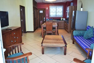 A spacious living area with a wooden dining table, chairs, a sofa, and a television.
